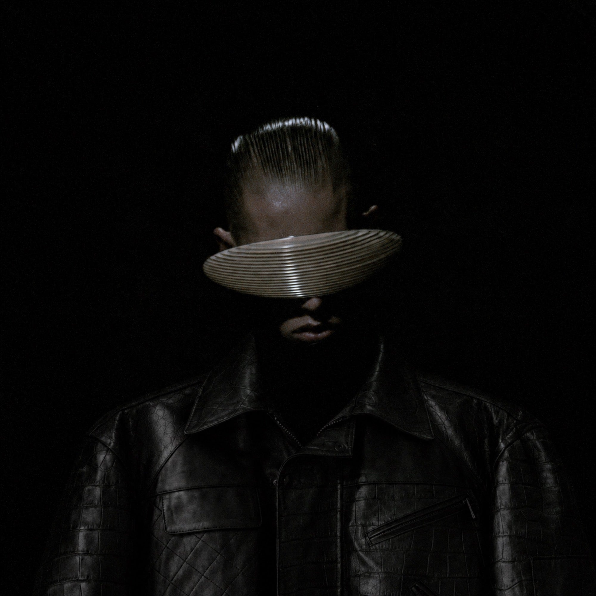 A man in croc-texture leather, face hidden by a ribbed visor, on black